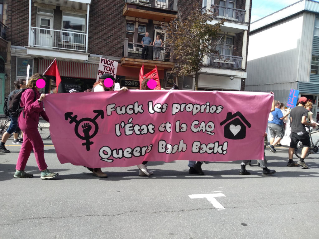 Plusieurs personnes tiennent une bannière disant "Fuck les proprios, l'état et la CAQ, Queers bash back!"